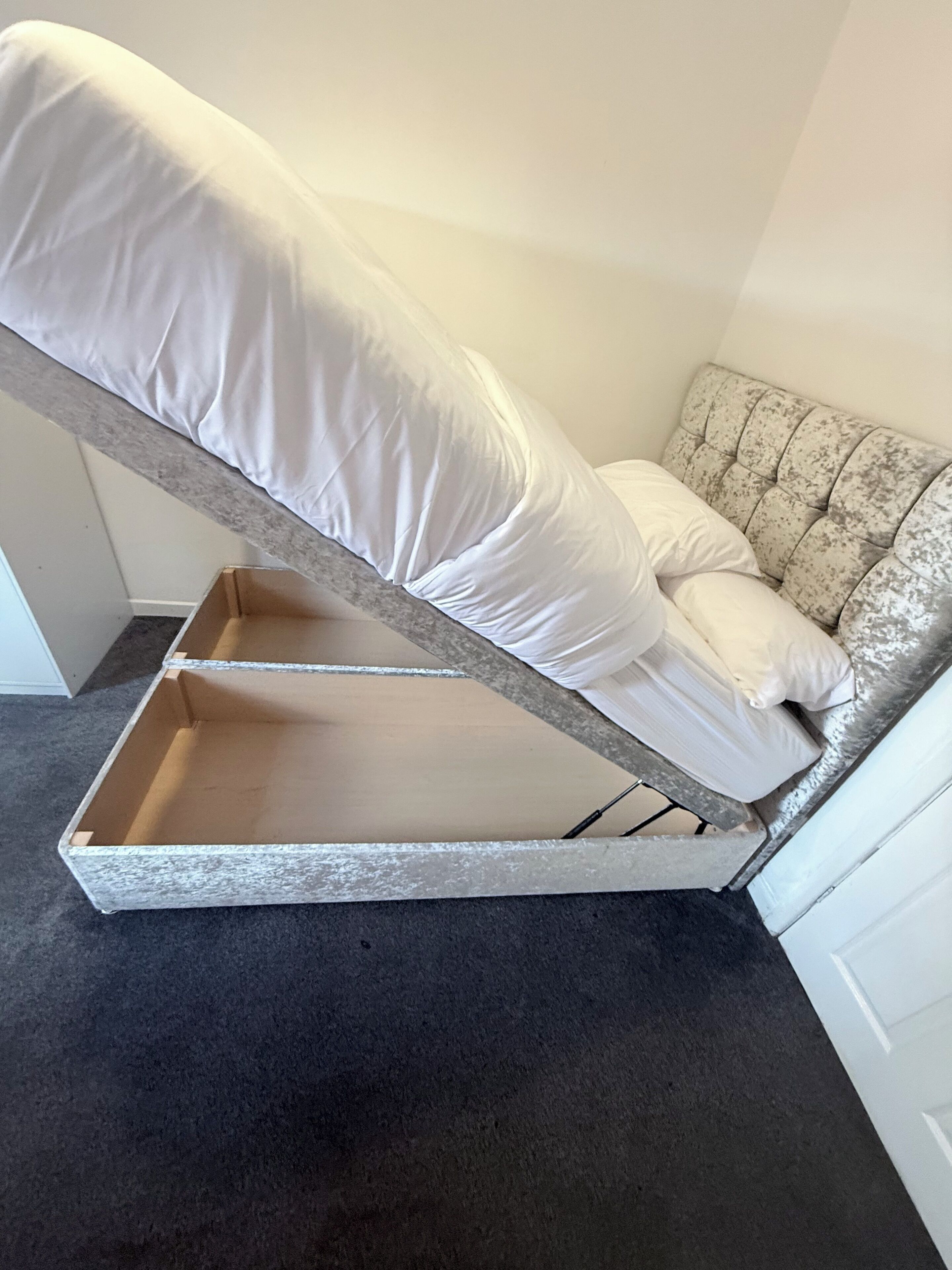 A corner room with a bed, a small table, and a chair.
