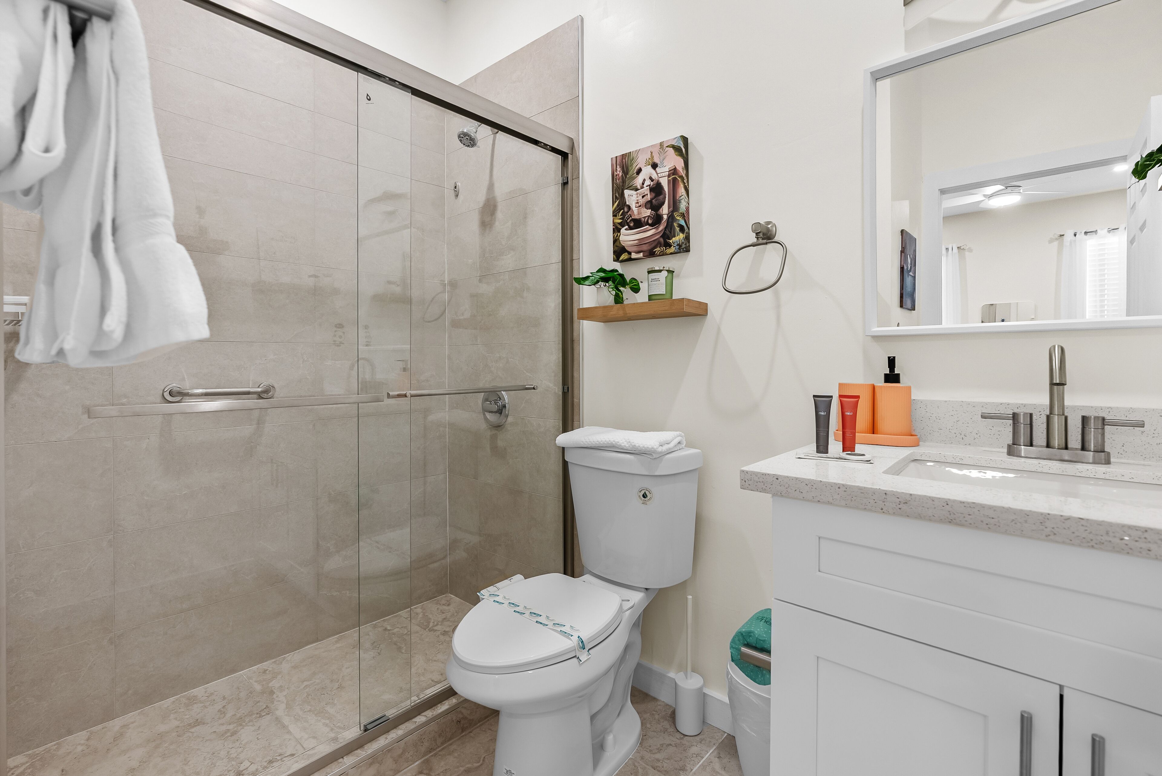 Ein modernes Badezimmer mit einer gläsernen Duschkabine, einer Toilette, einem Waschbecken mit Spiegel und einem Ablagefach für Pflegeprodukte.
