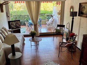 A room with a bed, a round table, a chair, and a view of an outdoor patio with chairs and a table.