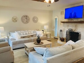Ein Wohnzimmer mit Sofa, Couchtisch, Kamin und Fernseher.