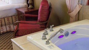 A bathroom with a bathtub, a red chair, a wooden nightstand, and a window with curtains. - Spacious 1BR Deluxe Villa w/ Full Kitchen, Balcony & Jetted Tub - 800 Sq Ft (Orlando)