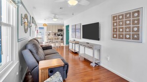 A modern living room with a gray sofa, wooden coffee table, ceiling fans, and a TV on a white stand. - Game Room | 3 Blocks 2 Beach | Linens + Towels (Seaside Heights)
