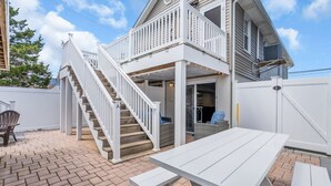 A two-story house with a white exterior, a covered patio, and a staircase leading to the upper level. - Game Room | 3 Blocks 2 Beach | Linens + Towels (Seaside Heights)