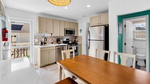 A modern kitchen with a wooden dining table, beige cabinets, a stainless steel refrigerator, and a hanging light fixture. - Game Room | 3 Blocks 2 Beach | Linens + Towels (Seaside Heights)