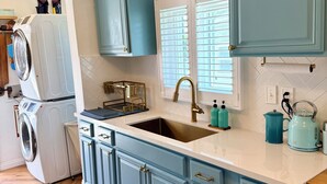 A kitchen with a built-in washing machine, a sink with a gold faucet, and teal cabinetry. - 0.5 Mile Walk To Sofi - Art Deco Beach Cottage - Entire Home (Inglewood)