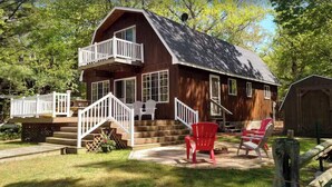 Een houten chalet met balkon, een trap naar de ingang en buitenmeubels.