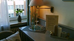 A hotel room with a window, a vase with flowers, a table with a lamp, a tray with a glass, and a menu on the wall. - City Hotel Deutsches Haus (Hagen)