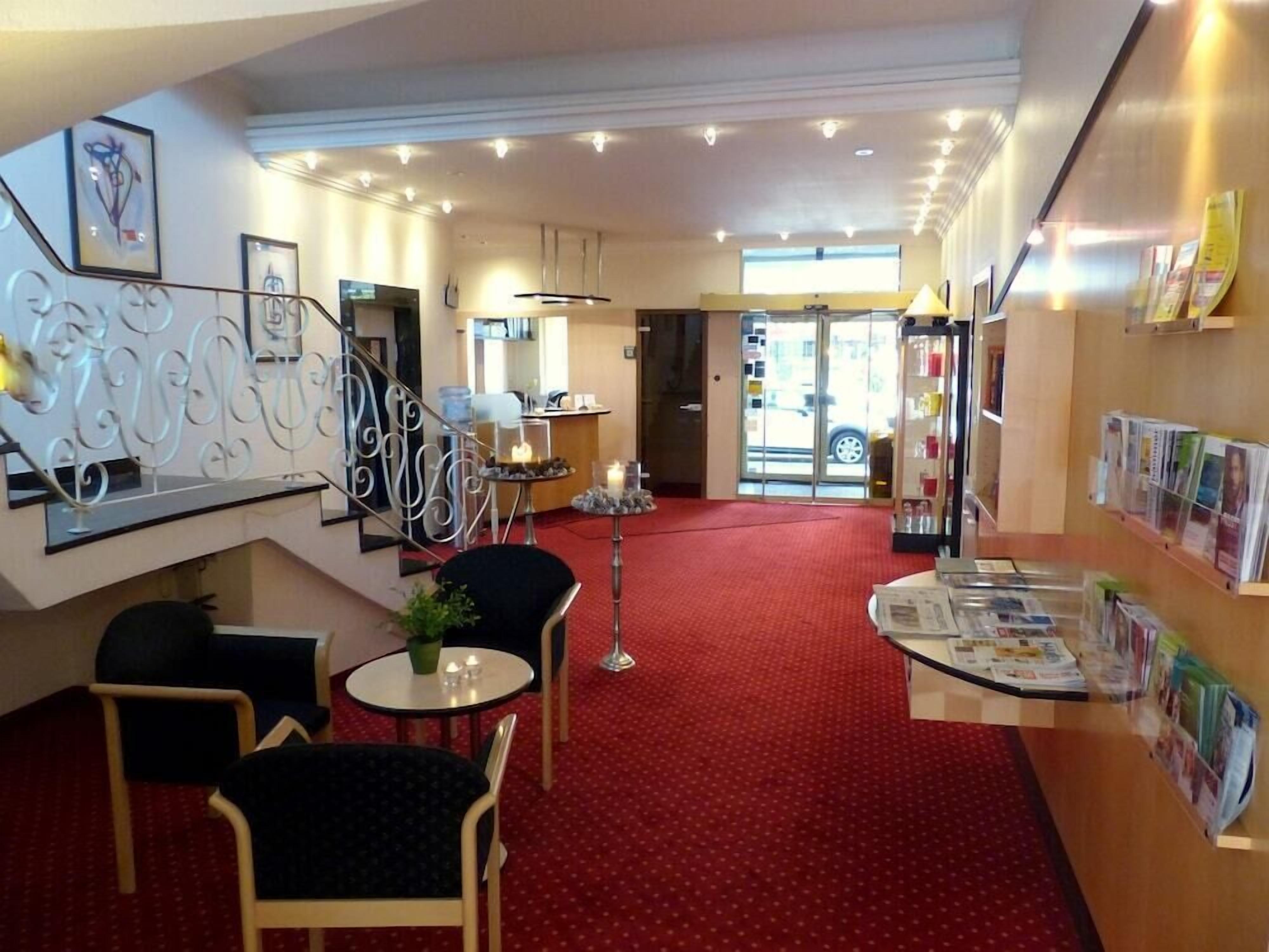 Eine Hotelhalle mit rotem Teppich, einer Rezeption, einer Treppe und einer Wand mit Zeitschriften.