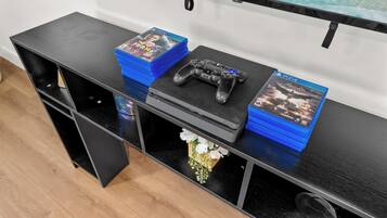 Eine schwarze Unterhaltungsanlage mit einer PlayStation 4 Konsole, einem Controller und mehreren Spielehüllen, darunter FIFA 21 und Batman Vengeance.