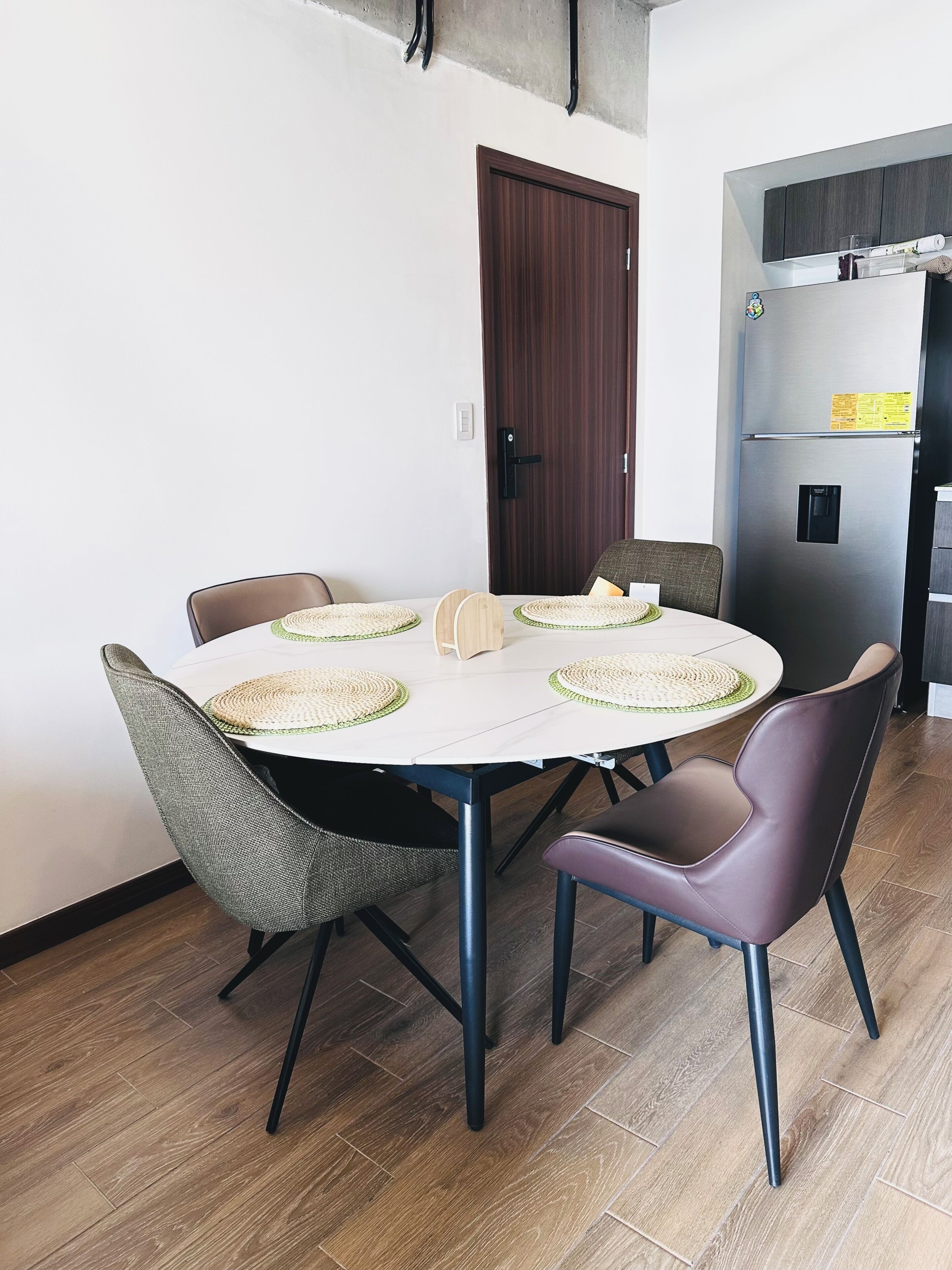 Un comedor con una mesa redonda, cuatro sillas y una puerta de madera al fondo.