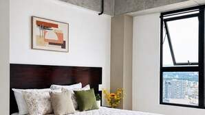 A modern bedroom with a large bed, a city view through a window, and a concrete ceiling. - Modern loft, excellent location and total comfort (Ciudad de Guatemala)