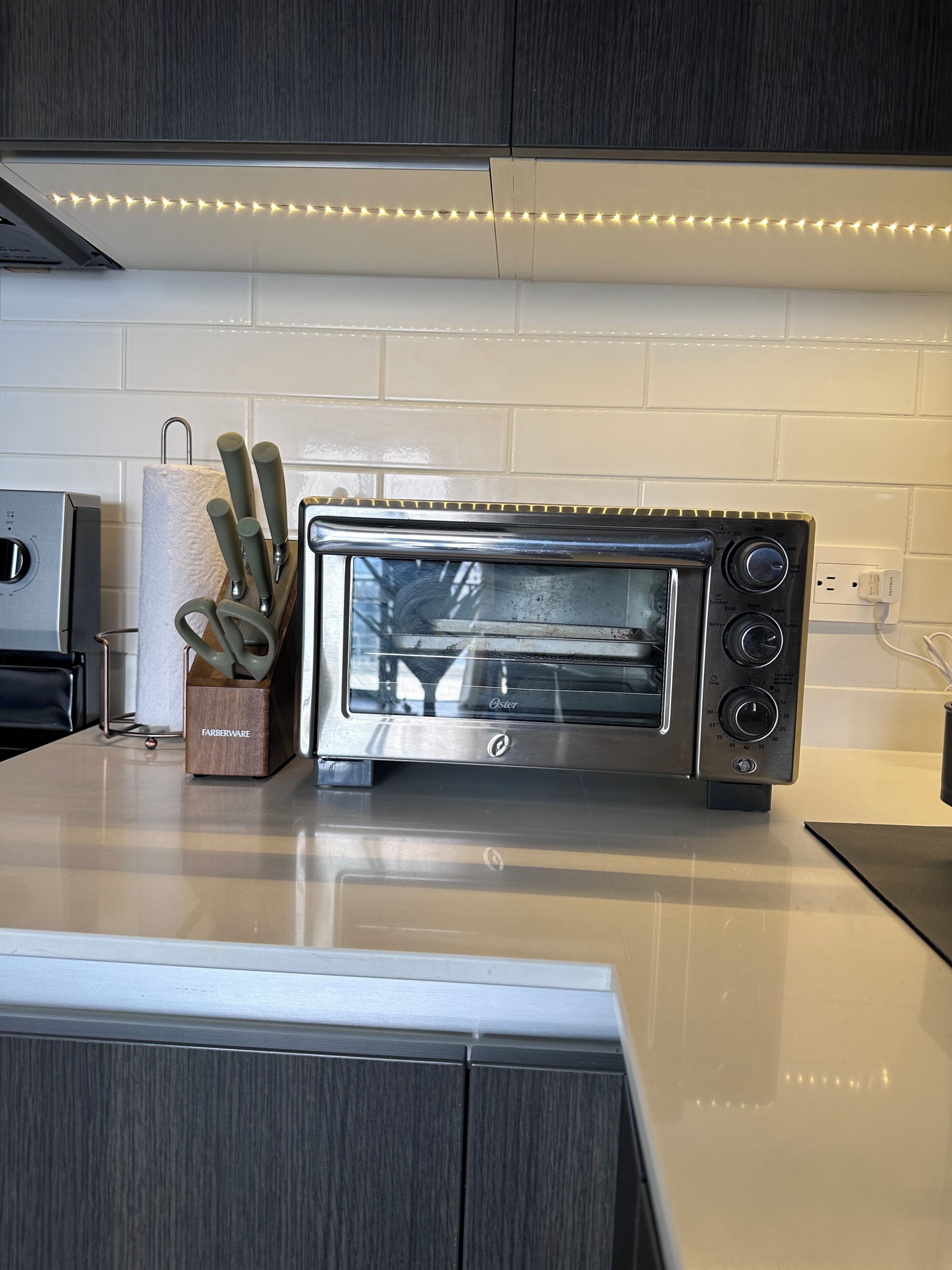 A modern kitchen with a built-in toaster oven, a knife block, and a white tiled backsplash.