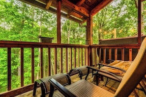 A wooden deck with outdoor seating, surrounded by a forest. - Hot Tub, Arcade, Sauna, Dog Run, 3 Kg Beds, Slp 12 (Pigeon Forge)