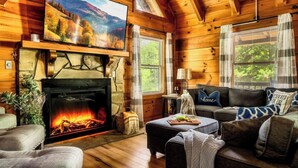 Ein Blockhaus-Interieur mit Kamin, Fernseher und einer Couch.