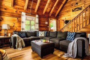 A log cabin interior with a sectional sofa, a small table with a fruit bowl, and a staircase. - Hot Tub, Arcade, Sauna, Dog Run, 3 Kg Beds, Slp 12 (Pigeon Forge)