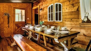 Ein Esszimmer aus Holz mit einem langen Tisch, gedeckt für vier Personen, Bänken und einem Fenster mit Vorhängen.