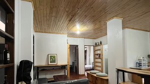 A room with wooden flooring, a black sofa, a wooden table, and a bookshelf.