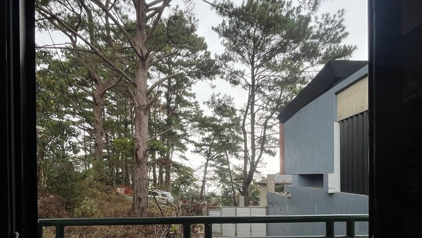 A balcony with a tiled floor, a metal railing, and a view of trees and a building.