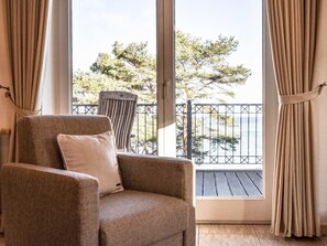 Una habitación con una ventana grande, una silla y vistas a árboles y un balcón.