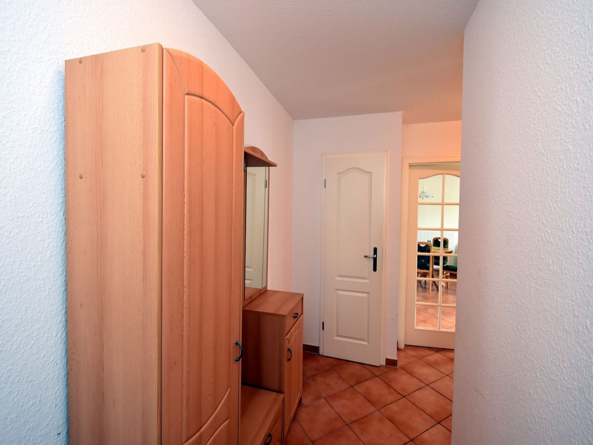 A hallway with a wooden wardrobe, a white door, and a tiled floor.