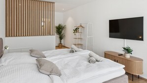 Ein modernes Schlafzimmer mit einem großen Bett, einem Fernseher, einer Holzkommode und einer Pflanze.