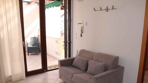 Una habitación con un sofá color beige, una puerta corrediza de vidrio que da a un espacio exterior, un interruptor de luz fijado a la pared y una toma de corriente.