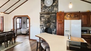 A kitchen with a stone fireplace, wooden cabinets, a built-in oven, and a dining area with a table and chairs.
