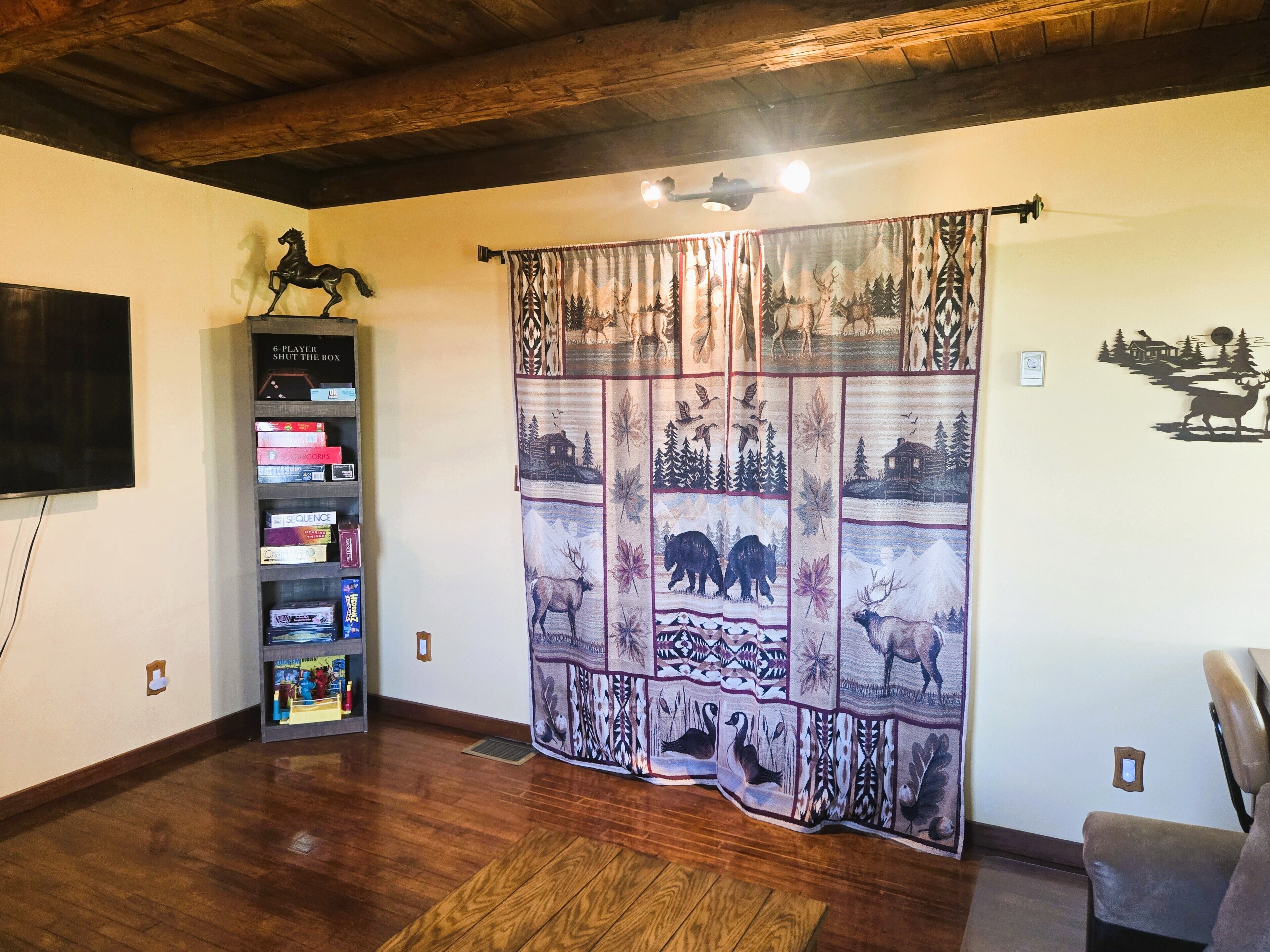 Un salon avec un plafond en bois, une bibliothèque, un téléviseur fixé au mur, un rideau à motifs et un motif décoratif sur le mur.