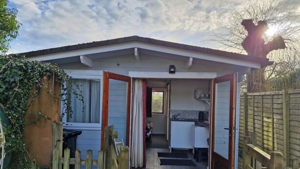A small, single-story building with a front door, a visible kitchen area, and a wooden fence.