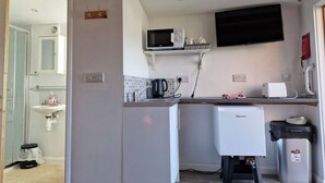 A compact kitchen with a microwave, kettle, and small refrigerator.