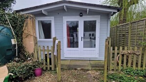 A small house with a white door and windows, surrounded by a wooden fence and a garden area with gravel and plants.