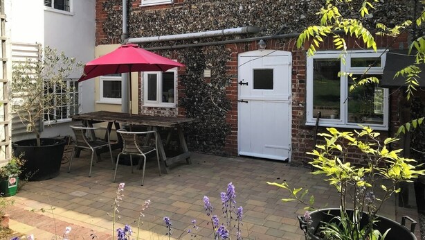Une terrasse avec une table et des chaises, un parasol rouge et des plantes en pot.