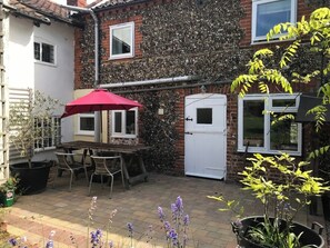 A patio with a table and chairs, a red umbrella, and potted plants. - Spacious Suffolk Cottage in Village Setting (Westleton)