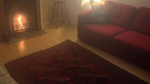 Un salon avec une cheminée, un canapé rouge, une lampe et un tapis à motifs.