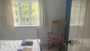 Une chambre à coucher avec un lit, un fauteuil à bascule, une fenêtre et une porte.