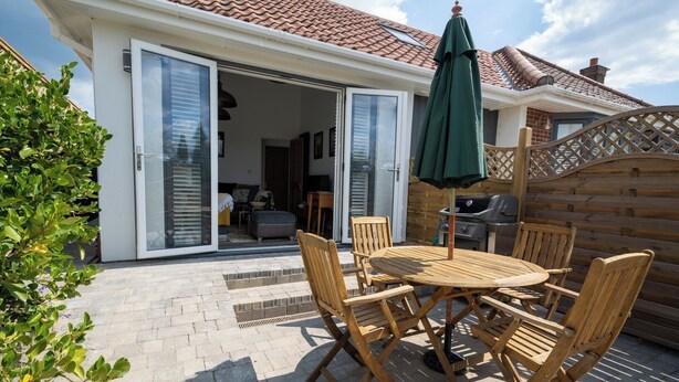 Une terrasse avec une table et des chaises, un barbecue et une porte-fenêtre coulissante donnant sur un espace intérieur.