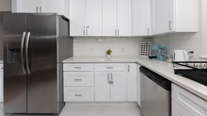 A modern kitchen with white cabinets, a stainless steel refrigerator, a dishwasher, and a coffee maker. - Comfortable 3BR/2BA Near Old Greenwich & Stamford (Stamford)