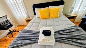 A neatly made bed with a grey blanket, a folded white towel, and a black item on top. There is a chair and a small table with a lamp. - Comfortable 3BR/2BA Near Old Greenwich & Stamford (Stamford)