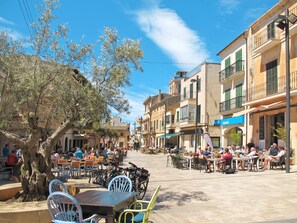 A sunny street with outdoor seating, trees, and buildings with balconies. - Apartment Oasis upper floor by Interhome (Santanyí)