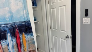 A room with a white door, a shelf with boxes, and a painting of surfboards on the wall. - Downtown Rehoboth Ave Renovated Condo Pet Friendly (Rehoboth Beach)