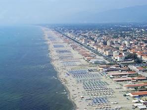 Eine Luftaufnahme einer Küstenstadt mit einem langen Strand, gesäumt von Reihen von Strandstühlen und Liegen.
