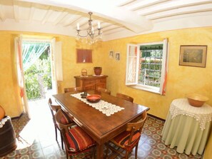 A dining room with a wooden table, chairs, a chandelier, a window with a view, and a small table with a bowl. - Casa Irene by Interhome (Colognora)