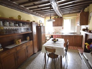 A kitchen with wooden cabinets, a dining table with chairs, and a hanging light fixture. - Casa Irene by Interhome (Colognora)
