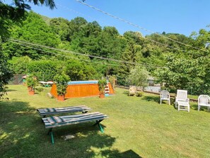 Un patio trasero con césped, una estructura de juego de madera, sillones de jardín y plantas en macetas.
