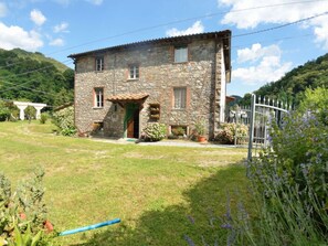 A stone building with a tiled roof, a small porch, and a garden with various plants. - Casa Irene by Interhome (Colognora)