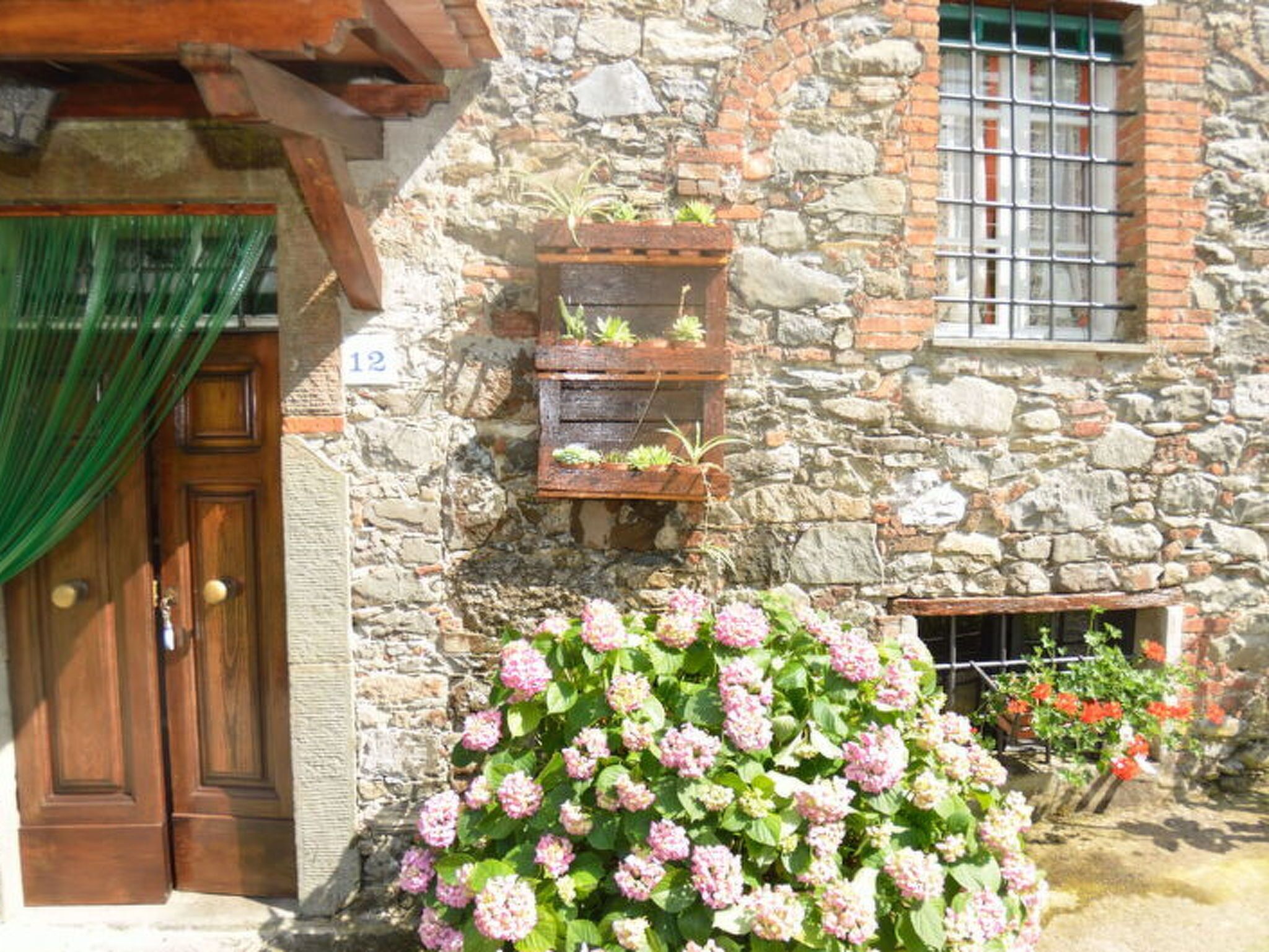 A stone building with a wooden door, a window with bars, and a flower box with plants.