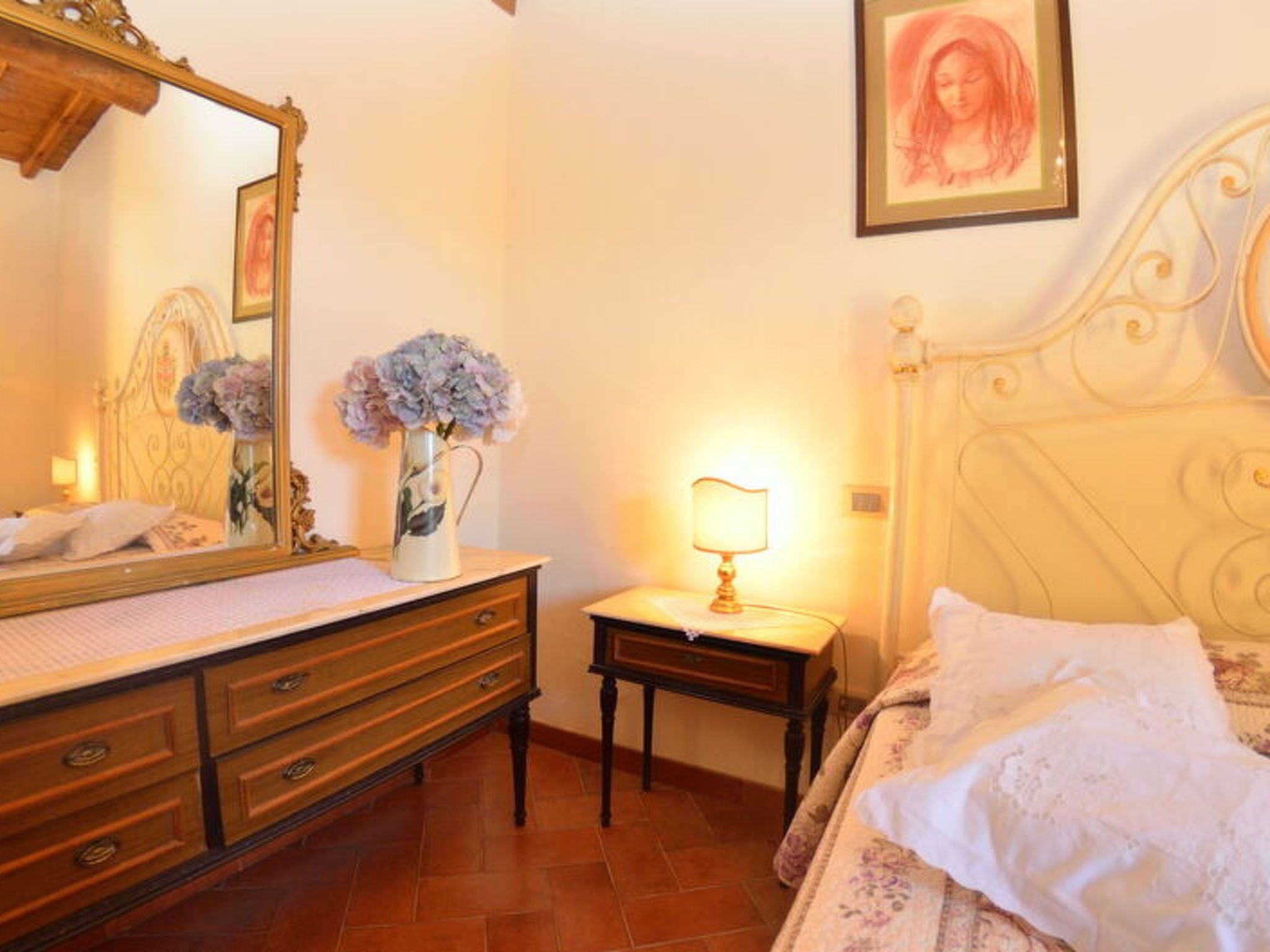 A bedroom with a bed, a dresser, a nightstand, a lamp, a mirror, and a framed picture on the wall.