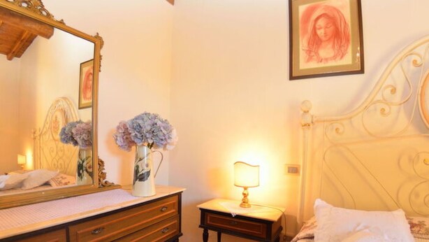 A bedroom with a bed, a dresser, a nightstand, a lamp, a mirror, and a framed picture on the wall. - La Capannella by Interhome (Capannori)