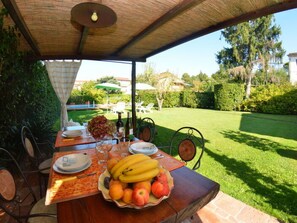 Ein Essbereich im Freien mit einem Tisch für zwei Personen, einer Obstschale und Blick auf einen gepflegten Garten.