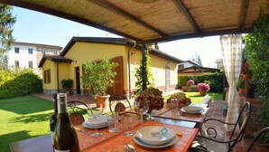 An outdoor dining area with a table set for two, a bottle of wine, and a garden view. - La Capannella by Interhome (Capannori)